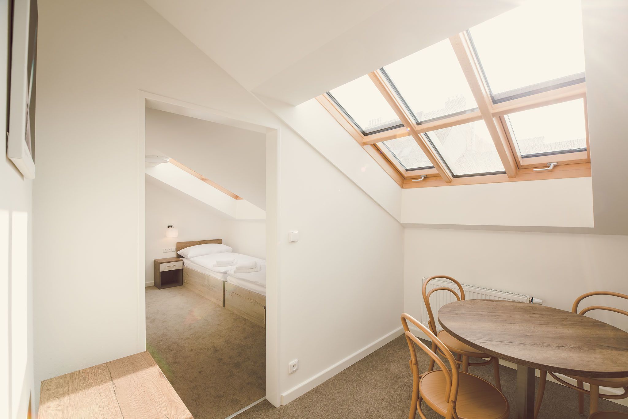 A room with a skylight, a bed, a small bedside table, and a round wooden table with chairs.