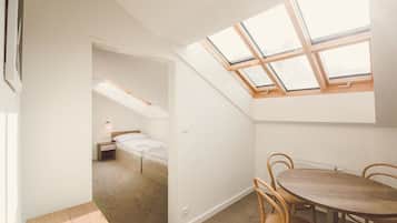 A room with a skylight, a bed, a small bedside table, and a round wooden table with chairs.