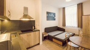 Quarto compacto com cozinha americana, cama com espaço de armazenamento, mesa de jantar e janela com cortinas.