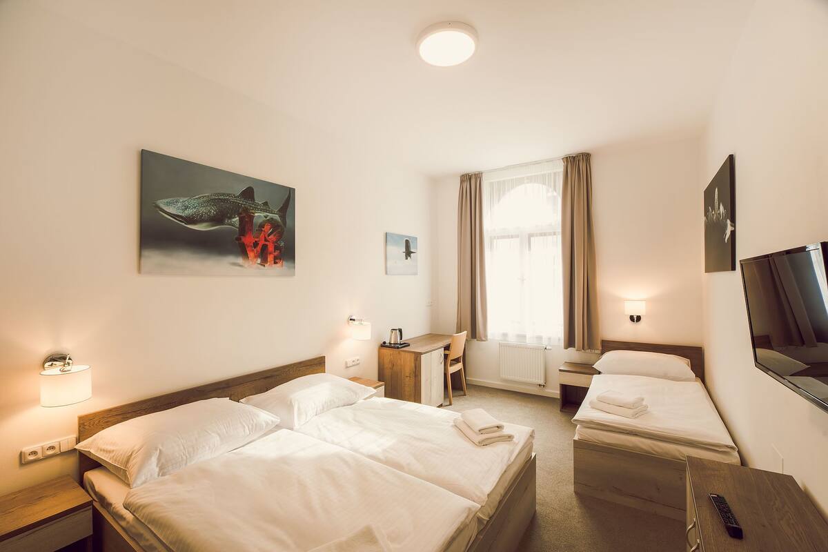 Habitación de hotel con dos camas, un escritorio, una silla, un televisor y obras de arte en las paredes.