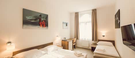 A hotel room with two beds, a desk, a chair, a TV, and artwork on the walls.