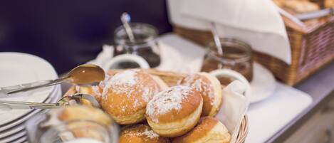 A buffet table with a basket of bread rolls, a milk jug, and a jar of jam.