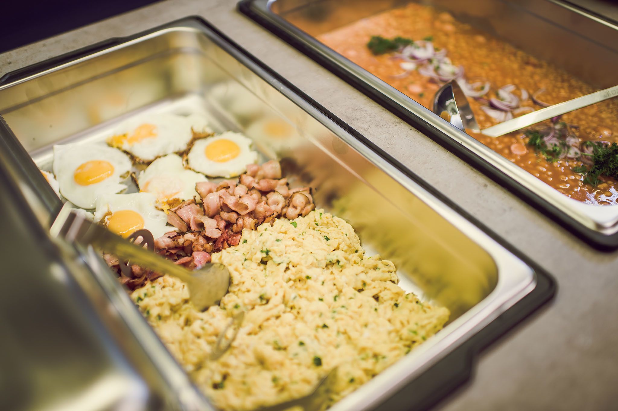 Un bufé con diversas opciones de comida, como huevos, tocino y arroz.