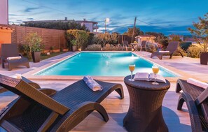 Zona de piscina con sillones de descanso y una mesa con bebidas y un libro.