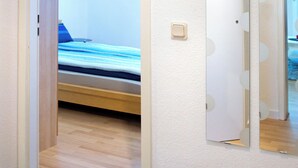 A narrow hallway leading to a bedroom with a bed and a wall-mounted mirror.