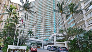 A hotel entrance with a sign reading "ILIKAI HOTEL," cars parked in front, and tall buildings with balconies and palm trees. - 20th Floor Ocean & Marina Views at The Ilikai! Washlet! FREE Parking & Wi-Fi! (Honolulu)