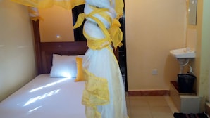 A bed with a canopy and a bedside table with a lamp and a basket. - Mali Guest House (Mombasa)