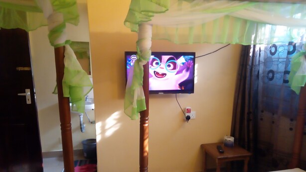 A hotel room with a bed, a television mounted on the wall, and a small table. - Mali Guest House (Mombasa)