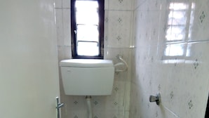 A small, tiled bathroom with a toilet, a window, and a sink. - Mali Guest House (Mombasa)