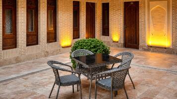 A courtyard with a round table and wicker chairs, surrounded by brick walls and wooden beams.