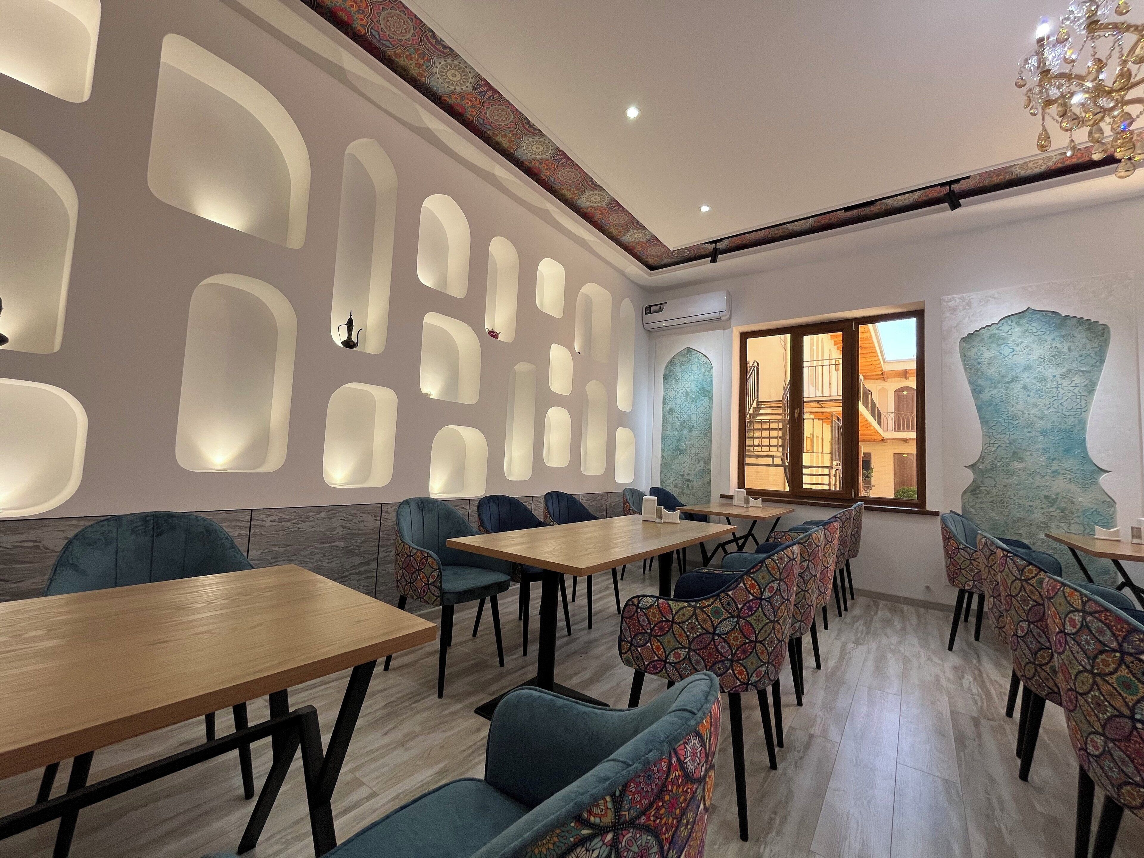 A modern restaurant interior with geometric wall designs, wooden tables, and patterned chairs.