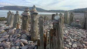 Een rotsachtig strand met houten palen waarop stenen gestapeld zijn.