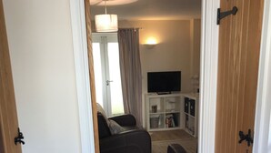 Een kamer met een bank, een televisie op een standaard, een houten vloer en een deur met een zwarte handgreep.