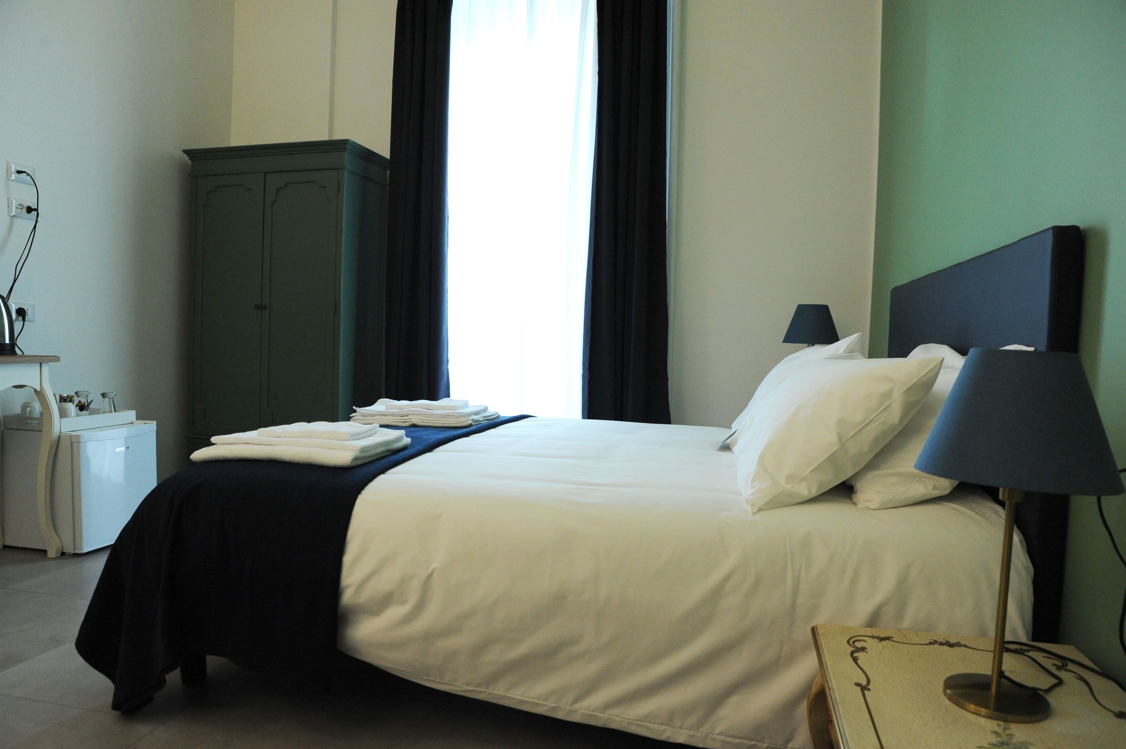 A hotel room with a bed, a nightstand, a lamp, and a wardrobe.