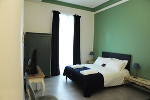 Une chambre d’hôtel comprenant un lit, un bureau, une chaise, une armoire et une fenêtre avec des rideaux.