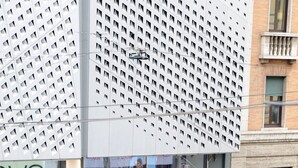 A modern building with a distinctive geometric facade, a visible store named 'OVS', and a parking sign indicating a 24-hour parking area. - Milano Dreams (Milan)