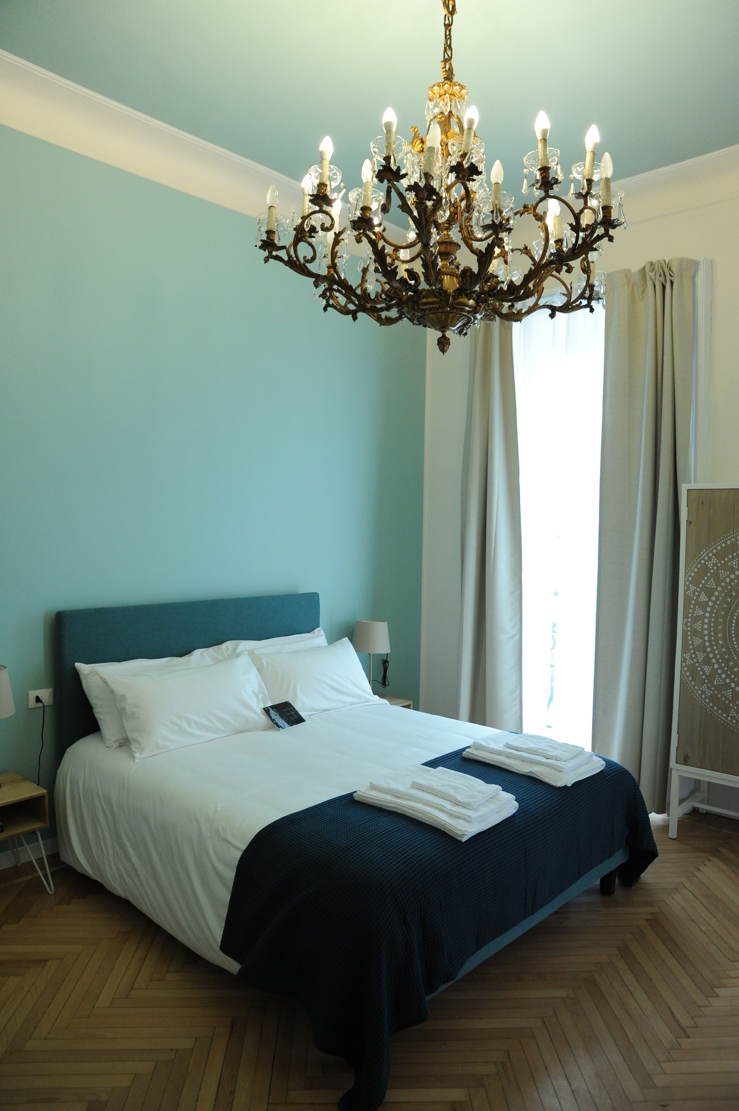 Una camera d'albergo con un grande letto, un lampadario, un pavimento in legno e vista all'esterno dalla finestra.