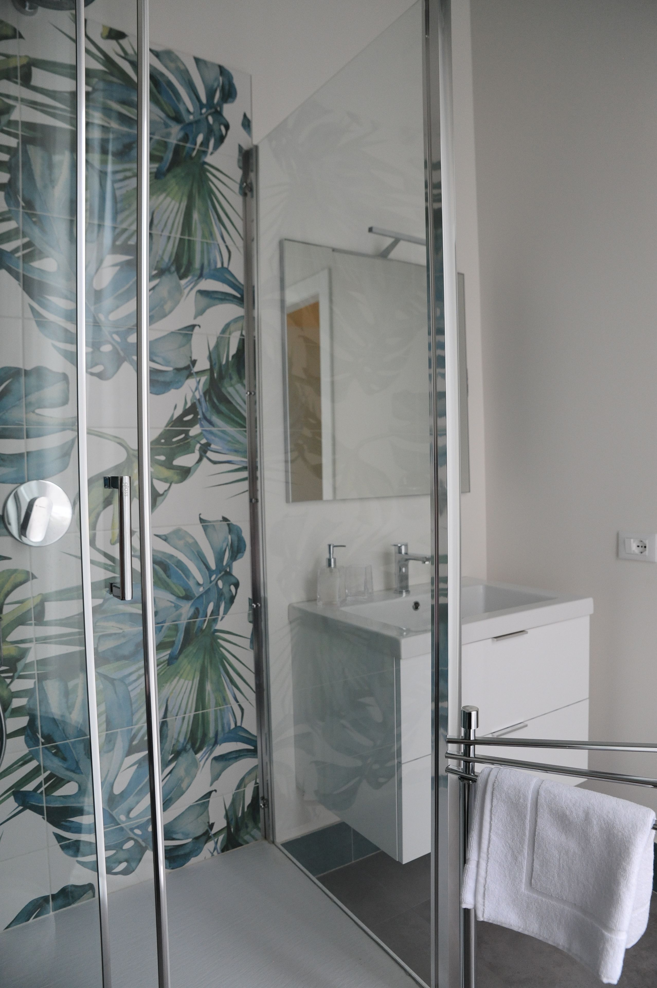 Een moderne badkamer met een douchecabine van glas, een witte wastafel en een spiegel boven de wastafel.