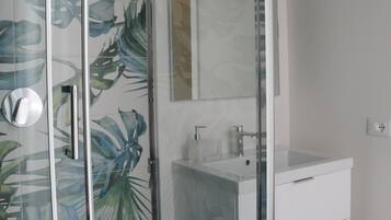 Een moderne badkamer met een douchecabine van glas, een witte wastafel en een spiegel boven de wastafel.