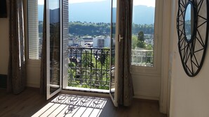 Ein Zimmer mit einer Schiebetür zu einem Balkon mit Metallgeländer, der einen Blick auf Stadt und Berge bietet.