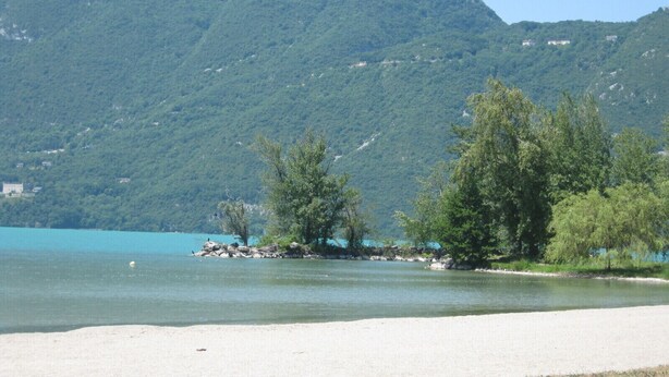 Ein Strand mit klarem Wasser, Bäumen und Bergen im Hintergrund.