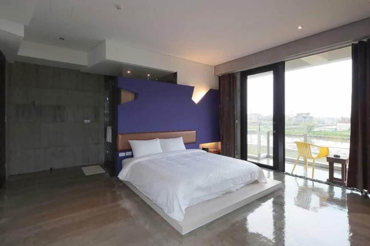 A modern bedroom with a large bed, a view of the city, and a balcony with a chair.