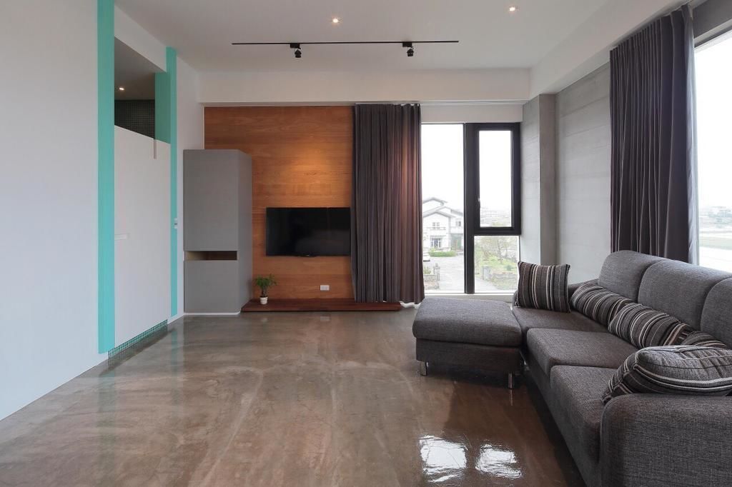 A modern living room with a grey sectional sofa, a flat-screen TV mounted on a wooden wall, and a large window with curtains.