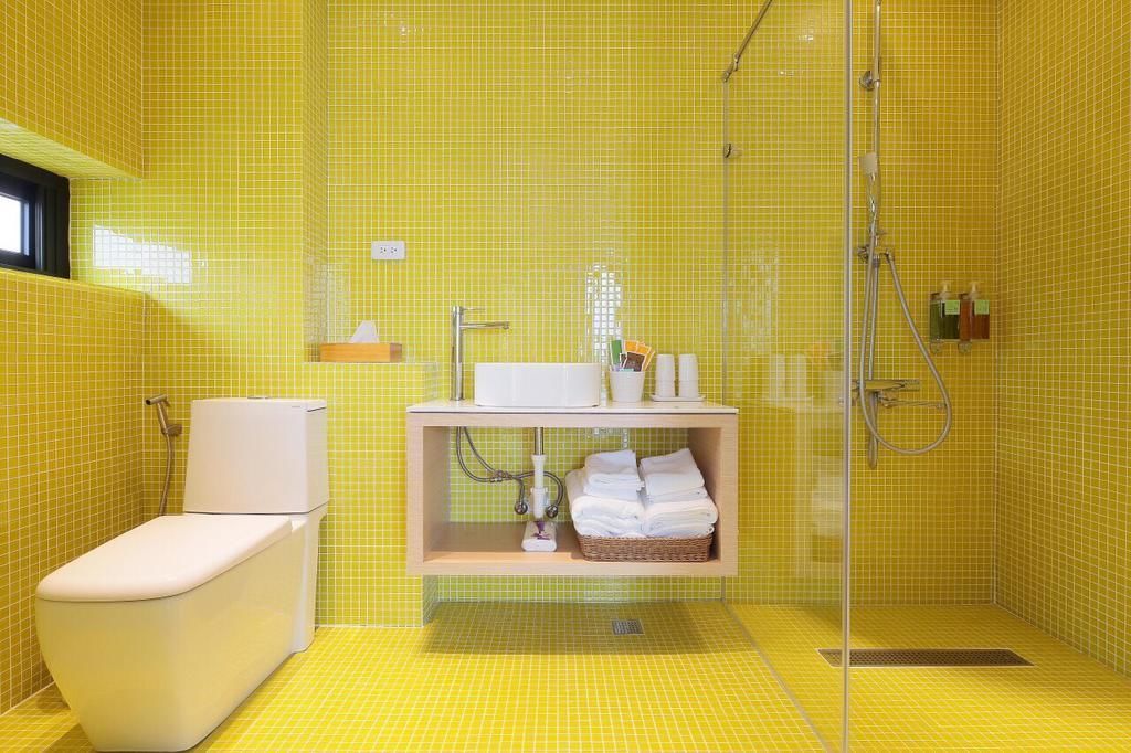 A bathroom with yellow tiles, a white toilet, a sink with a mirror, and a shower area.