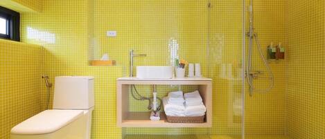 A bathroom with yellow tiles, a white toilet, a sink with a mirror, and a shower area.