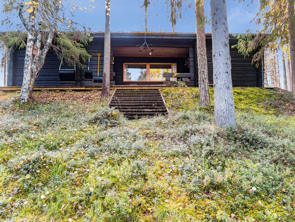 A modern log cabin with a wooden staircase leading to a large window.
