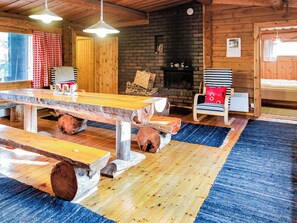 A rustic interior with a wooden dining table, benches, a fireplace, and a striped chair.