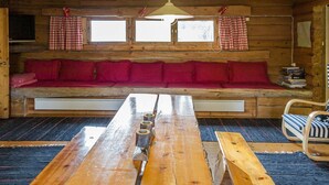 En stuga med träpanel på insidan, med en träbänk, ett bord och en soffa med röda kuddar.