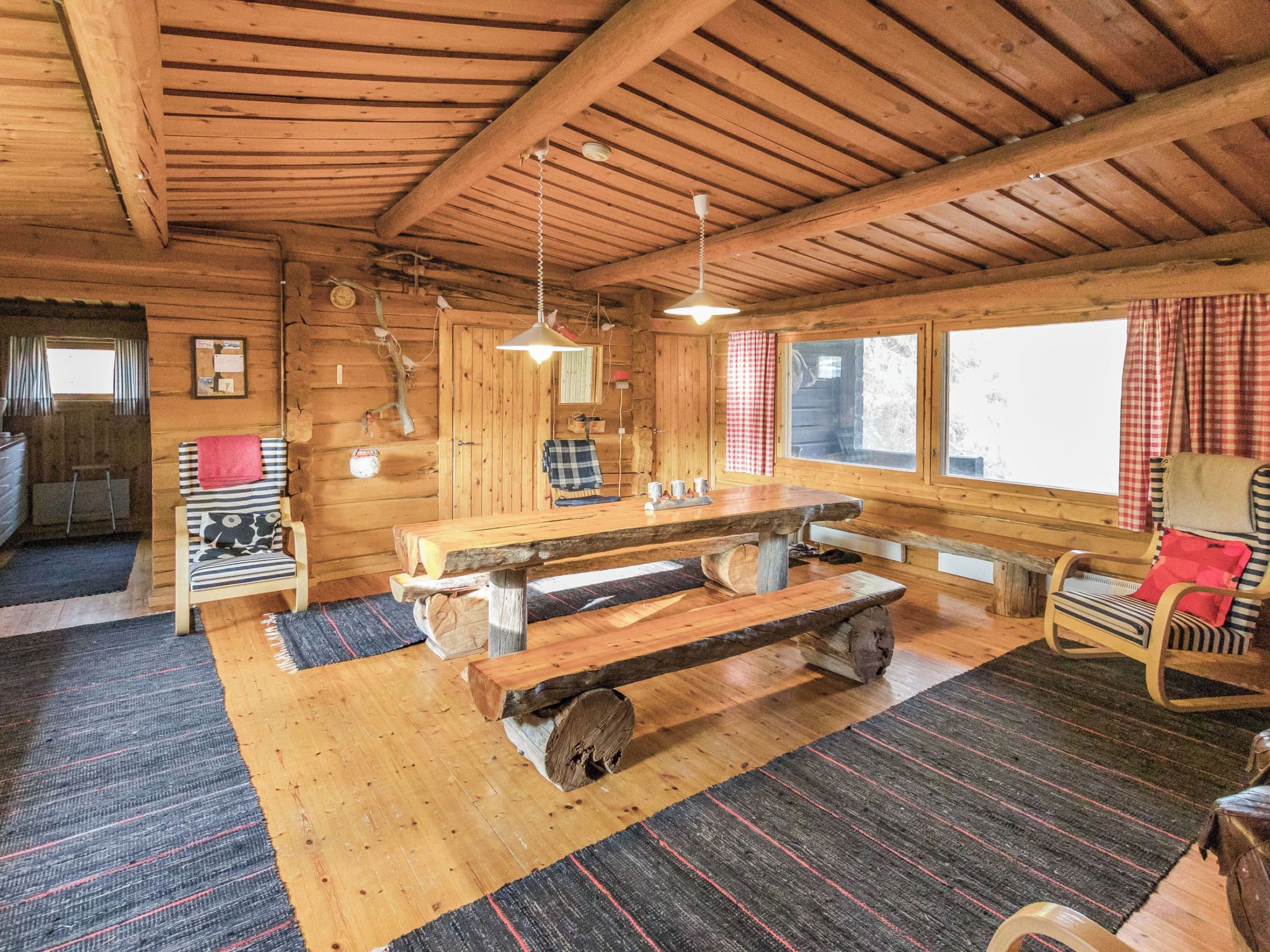 Interior rústico de cabana com mesa de jantar de madeira, bancos, uma cadeira de balanço e lareira.
