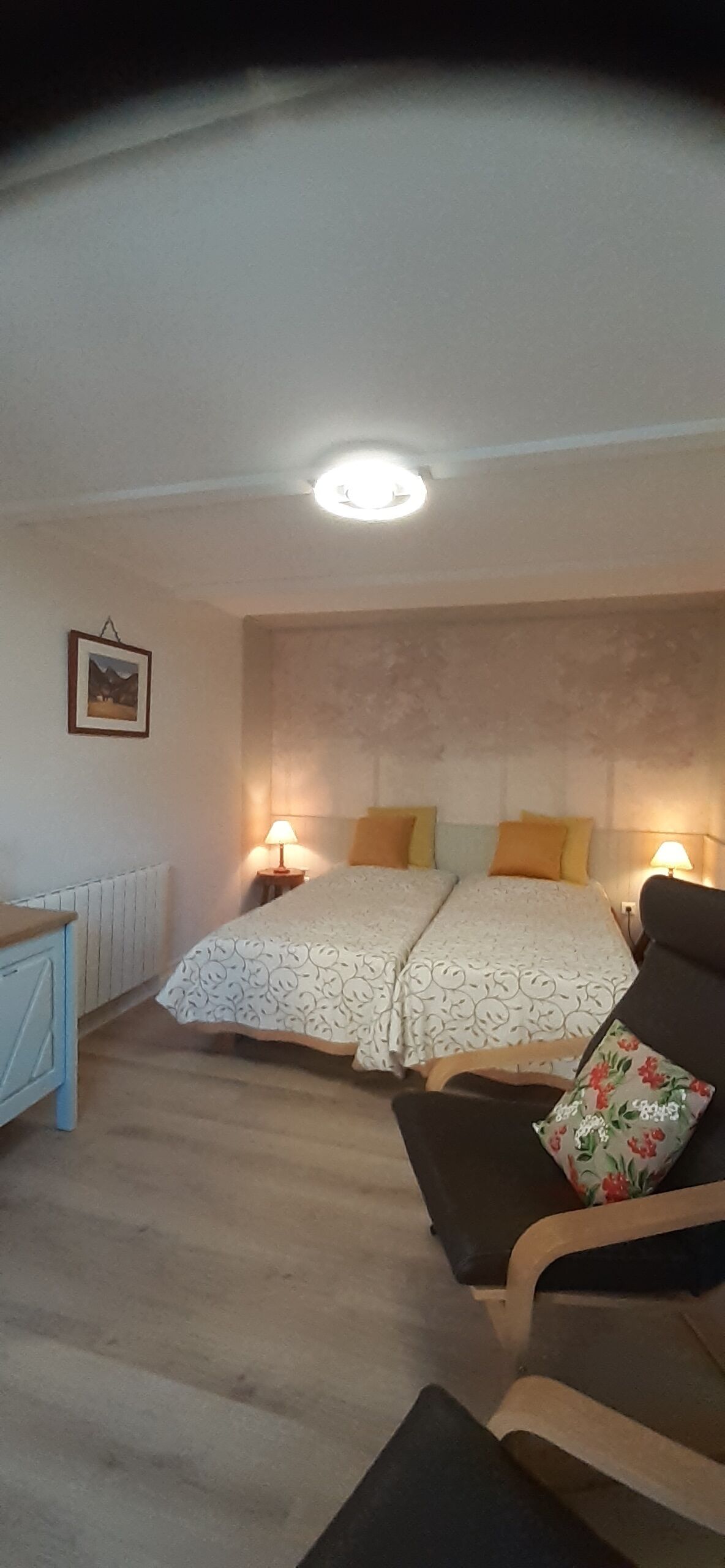 Un dormitorio con una cama doble, lámparas de noche, una silla, una mesita y un cuadro en la pared.