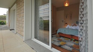A bedroom with a bed, a nightstand, a lamp, and a window with a view of a building.