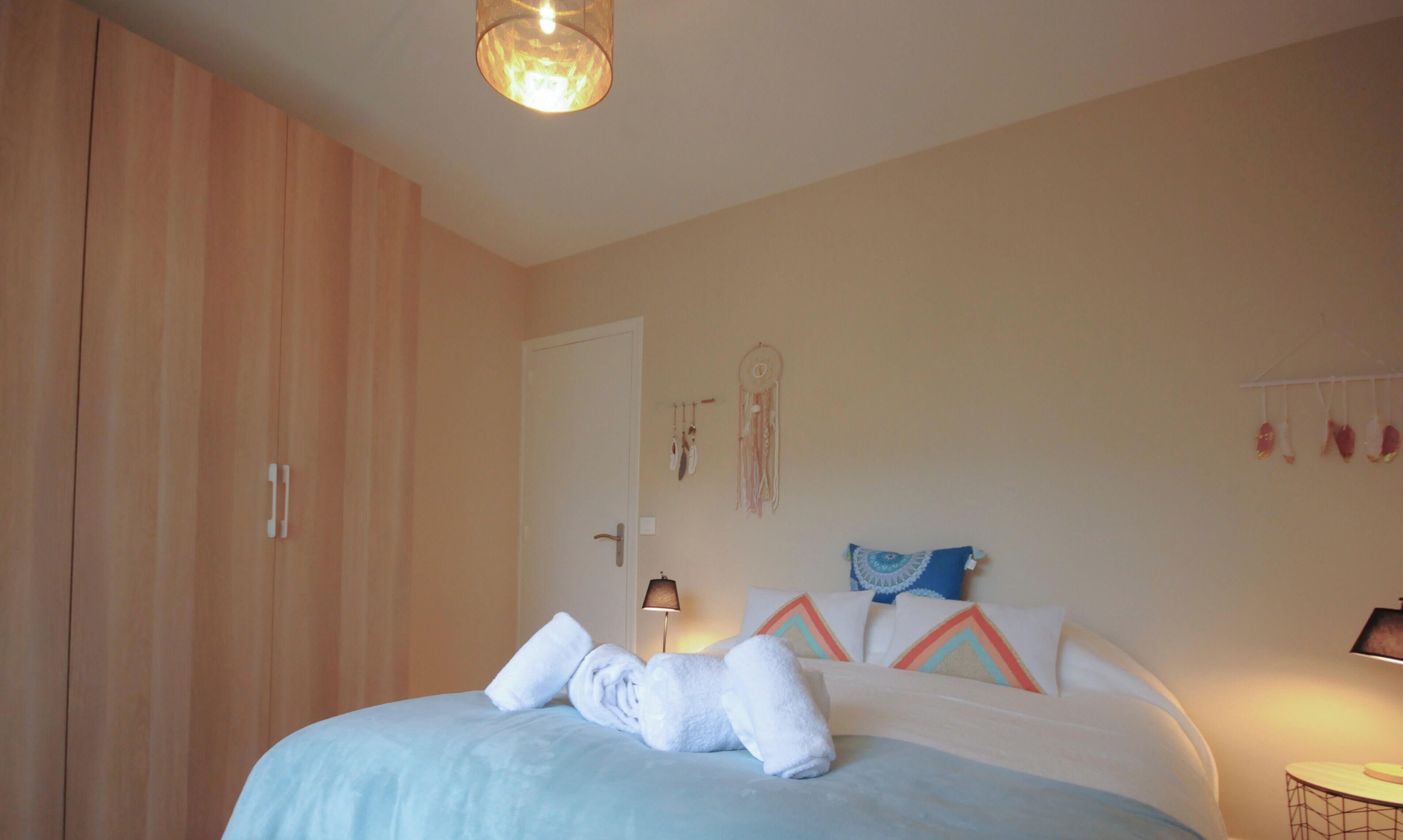 Une chambre à coucher comprenant un lit, une armoire, une table de chevet et un mur orné d’un attrape-rêves et de décorations suspendues.