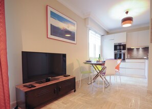 Una sala de estar moderna con televisor de pantalla plana, un mueble de madera y una zona de comedor con mesa y sillas.