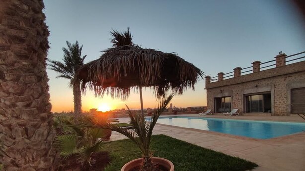 A pool area with a sunset view, a thatched umbrella, and a stone building. - Luxury villa with private pool not overlooked. (Fès)