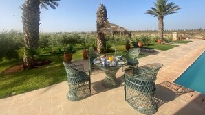 A poolside area with a round table and chairs, surrounded by palm trees and potted plants. - Luxury villa with private pool not overlooked. (Fès)