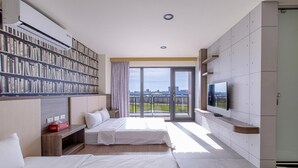 Une chambre d’hôtel moderne dotée d’une grande bibliothèque, d’un téléviseur à écran plat et d’un balcon offrant une vue sur la ville.