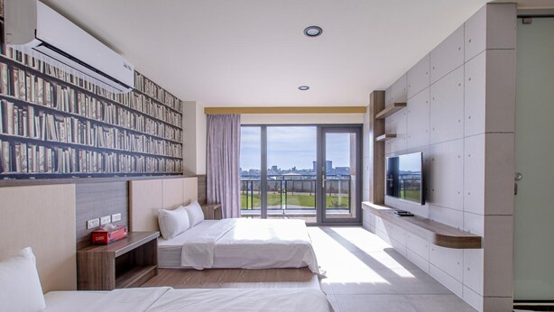 A modern hotel room with a large bookshelf, a flat-screen TV, and a balcony with a city view. - Sharp bnb (Magong)