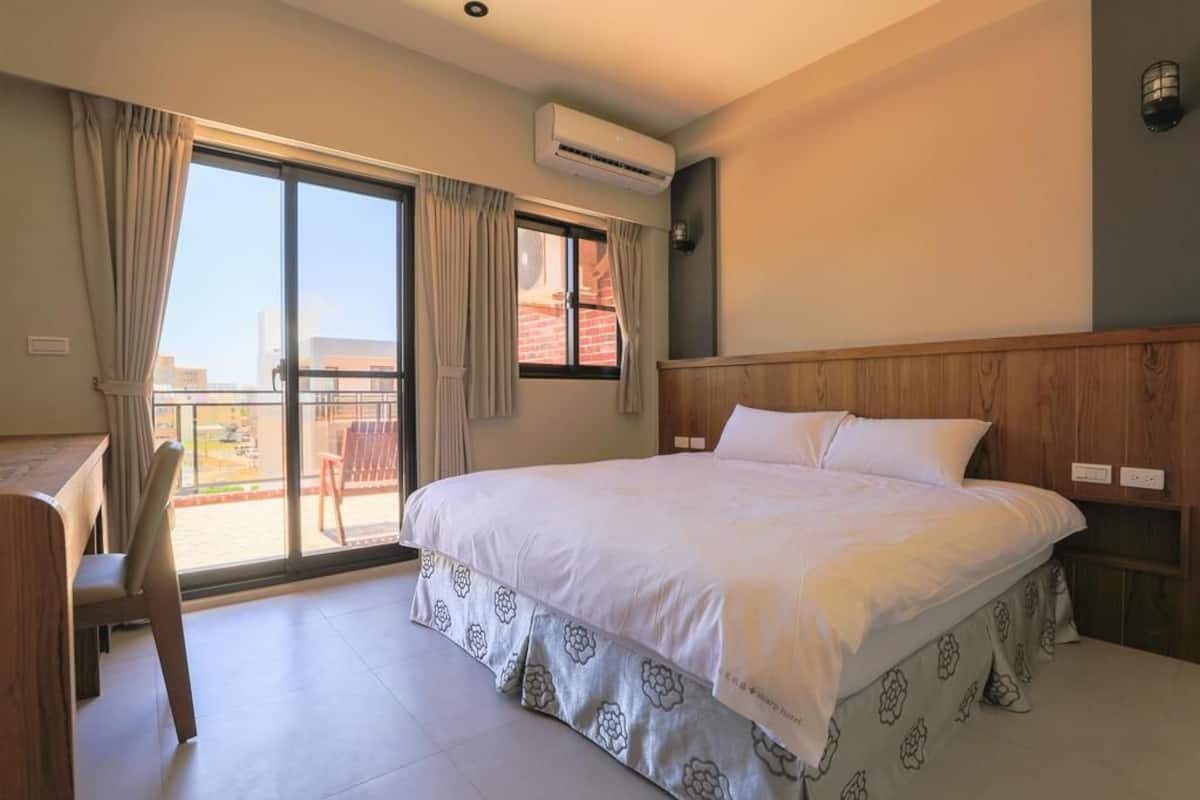 Habitación de hotel con cama, escritorio y silla. Se ve una ventana con cortinas y un equipo de aire acondicionado encima.
