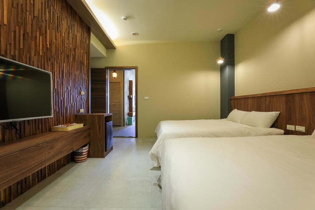 Habitación de hotel con televisión sobre un soporte de madera, dos camas y un panel de pared de madera.