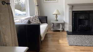 A bedroom with a bed, a bedside table with a lamp, a fireplace, and a window with curtains. - Cosy 3 bed holiday home (Kenmare)