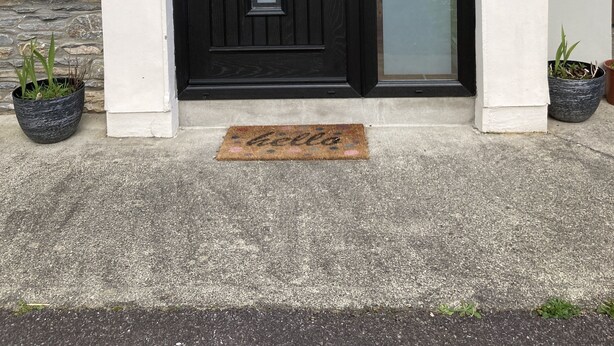 A black front door with a glass panel, a white number '7' on the wall, and two potted plants on either side. - Cosy 3 bed holiday home (Kenmare)