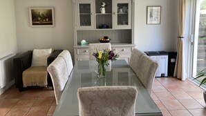 A dining area with a glass table, four chairs, a cabinet with glass doors, and a window with curtains. - Cosy 3 bed holiday home (Kenmare)