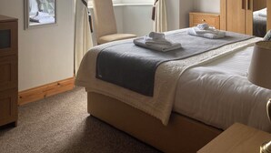 A bedroom with a large bed, a wooden wardrobe, a bedside table, a chair, a window with curtains, and a ceiling light. - Cosy 3 bed holiday home (Kenmare)