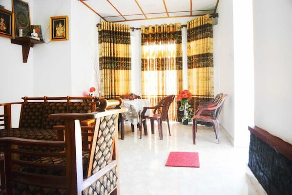A dining area with a table and chairs, a red mat on the floor, and a window with striped curtains.