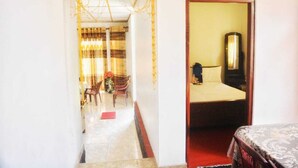 A hotel room with a bed, a mirror, and a small table. There is a hallway leading to another room with a chair and a table. - Mount view family rest & cottage (Hildummulla)