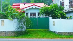 A residential area with a house featuring a red roof, a green gate, and a white wall with a stone base. - Mount view family rest & cottage (Hildummulla)
